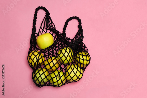 Black mesh shopping bag with organic green apples on pink background. Image with copy paste, top view.