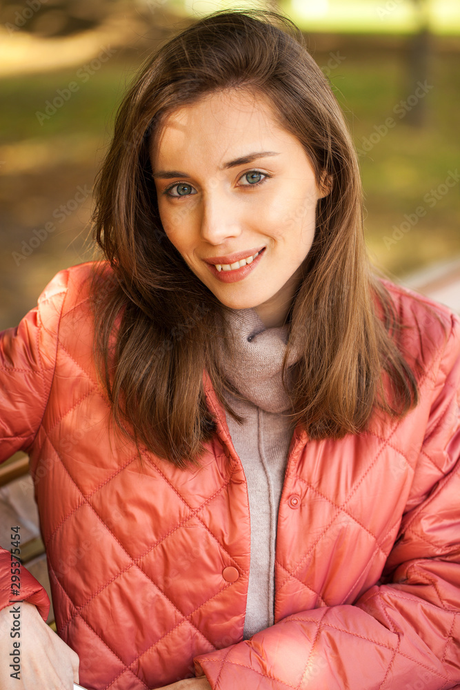 Young stylish woman in a salmon down jacket posing on a background of autumn park Young stylish woman in a salmon down jacket posing on a background of autumn park