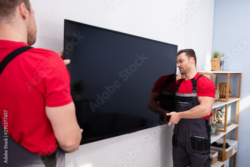 Male Movers Fixing The Large LCD Television On Wall