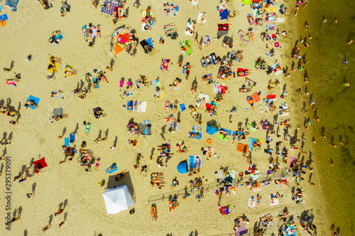 Top view of a sandy beach filled with people. Crowds of people swim and sunbathe on the Baltic Sea on a hot sunny day. Beach in Gdynia, Poland. 