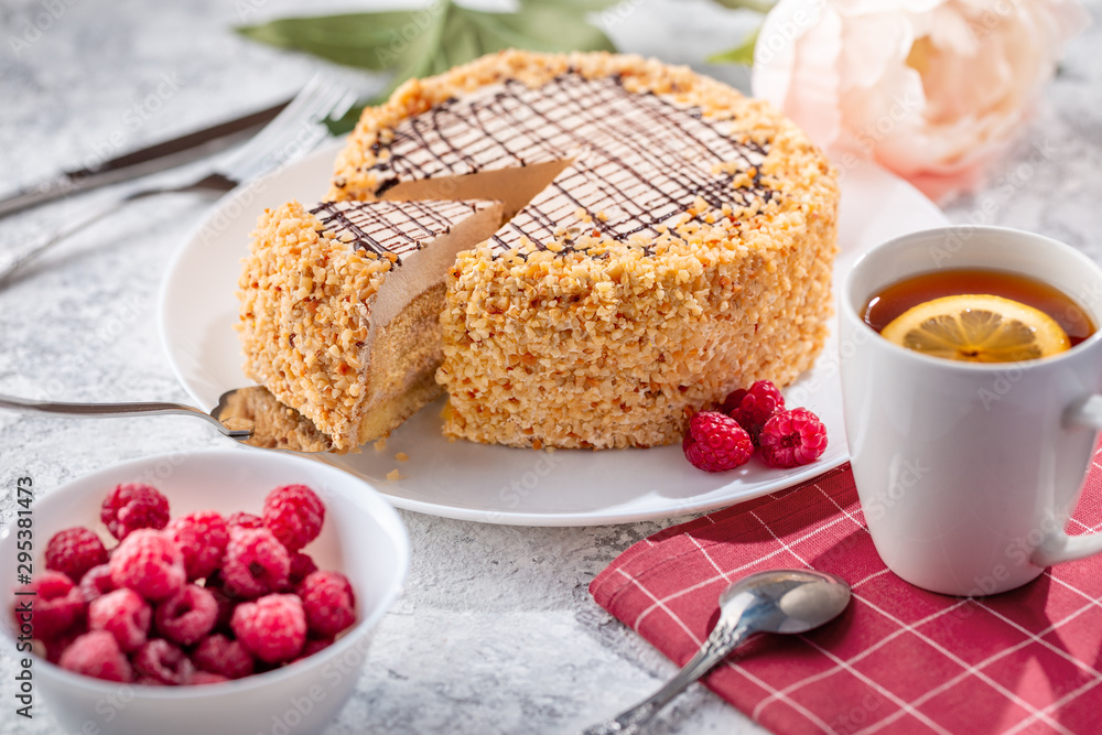 Sponge biscuite cake with cream lies on a plate. On the table are berries, a cup with tea and a spoon, a napkin. Sponge biscuite cake with cream lies on a plate. On the table are berries, a cup with tea and a spoon, a napkin.