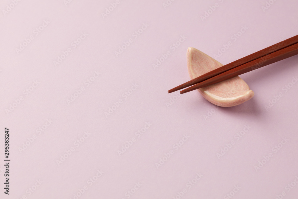 Wooden chopsticks and chopstick rest on bright paper background. Close up. Copy space. Wooden chopsticks and chopstick rest on bright paper background. Close up. Copy space.