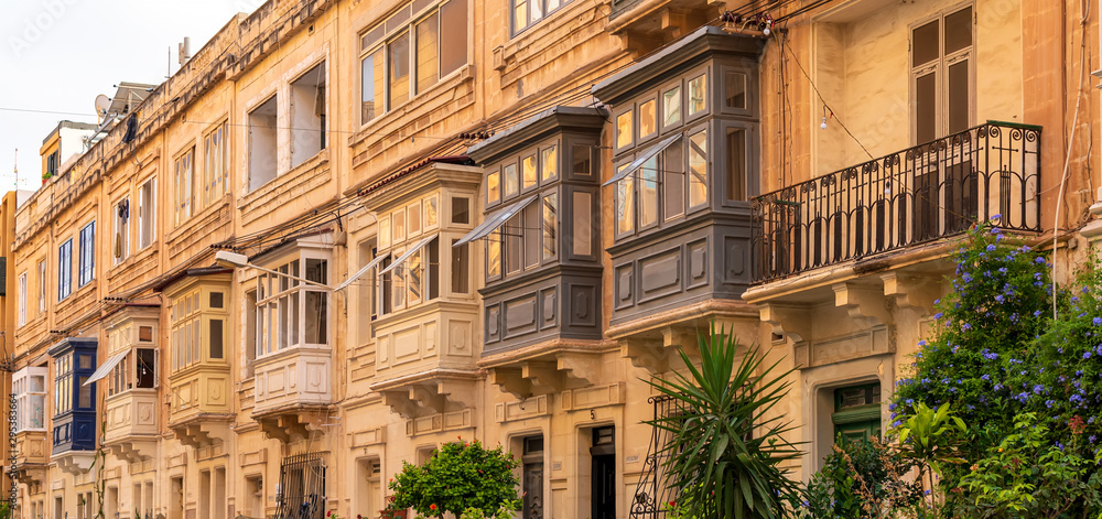 Residential house facade with traditional Maltese wooden balconies in Sliema, Malta, coloured in orange with evening sunlight. Authentic Maltese urban scene.