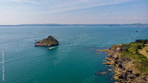 An aerial panorama view of a rocky island surrounded by beautiful flat blue sea water with rocky coastline under a majestic blue sky and some white clouds