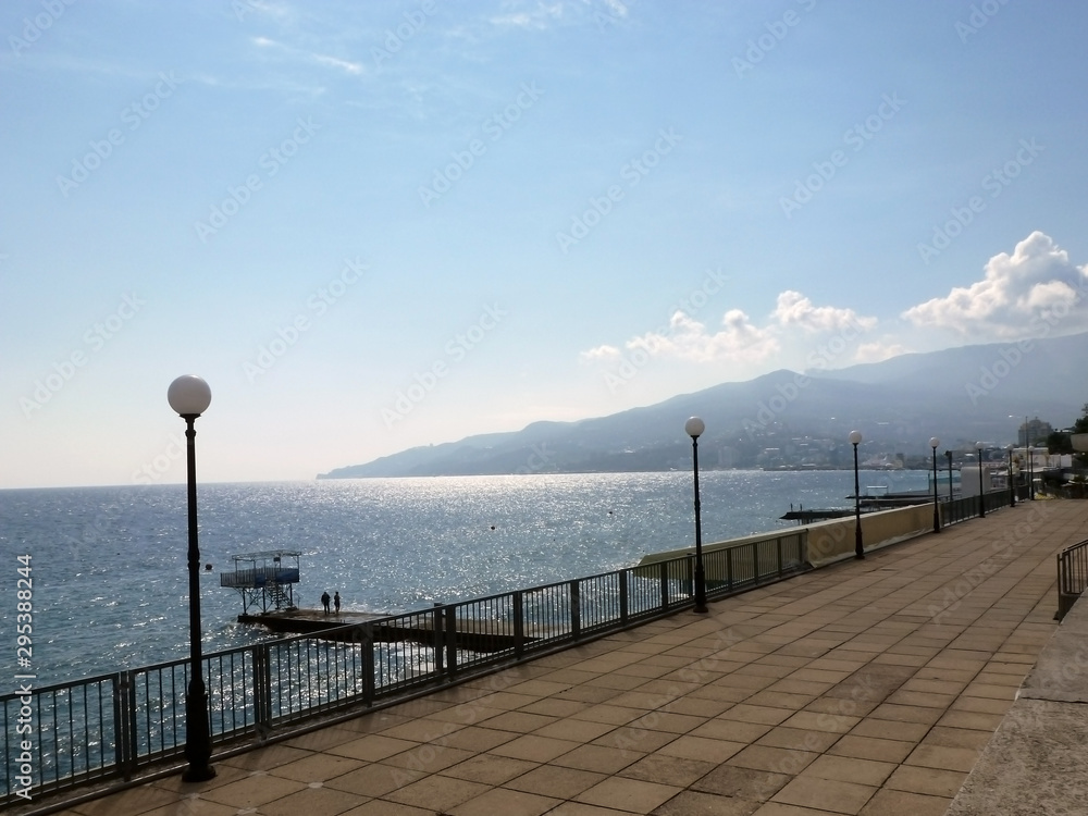 Empty sea embankment with lanterns on a sunny bright day. In the background mountains and settlement
