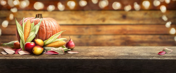 Thanksgiving celebration banner of pumpkins, apples, pears and corncobs on the left hand side of a table with a wooden background.