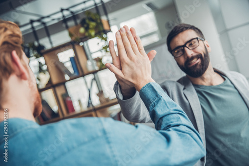 Male startupers working together at office standing giving high five smiling friendly photo