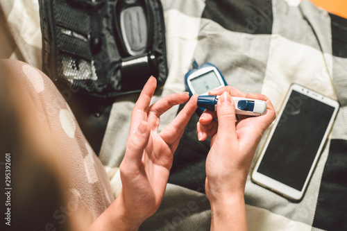 Theme diabetes. A close-up macro plan. Hands of a young Caucasian woman at home in the bedroom on the bed. It uses the technology of an instrument for measuring the level of glucose in the blood