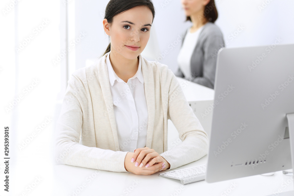 Business woman working with computer in office, female colleague at background. Headshot of Lawyer or accountant at work while sitting at the desk Business woman working with computer in office, female colleague at background. Headshot of Lawyer or accountant at work while sitting at the desk