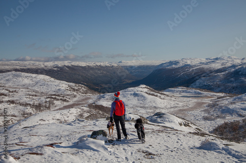 Girl with red backpack and two dogs are looking at snow covered mountain peaks