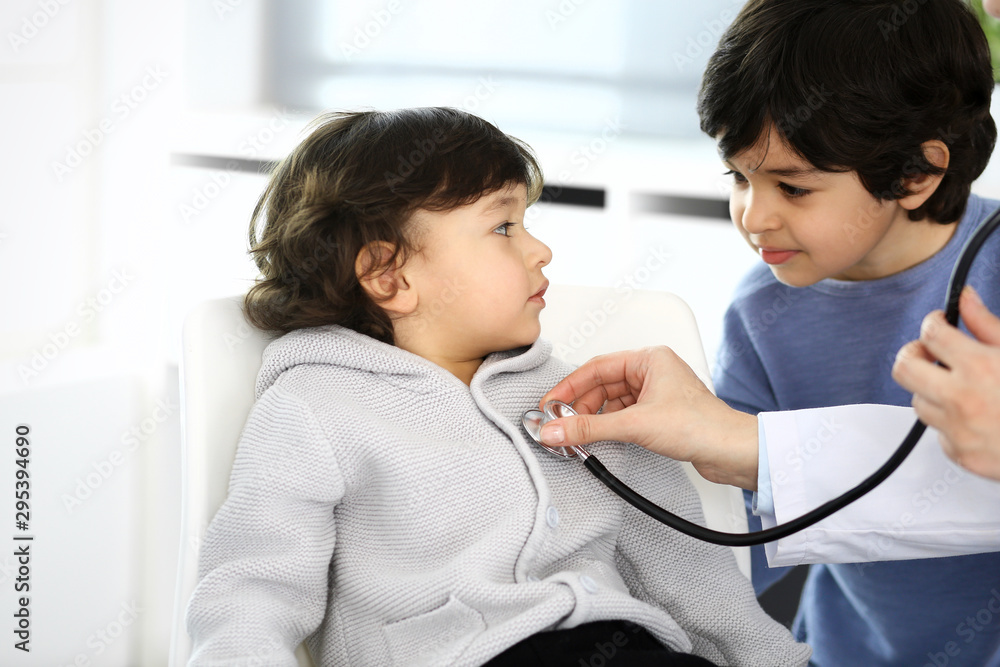Obraz premium Doctor examining a child patient by stethoscope. Cute arab boy at physician appointment. Medicine and healthcare concept