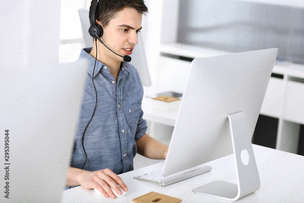 Group of operators at work. Call center. Focus on young man receptionist in headset at customer service. Business concept and casual clothing style Group of operators at work. Call center. Focus on young man receptionist in headset at customer service. Business concept and casual clothing style