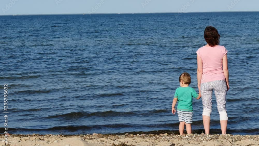 Mom playing with little child boy on seashore. Adult woman and her son enjoying summer day on beach. Family vacation at sea. Slow motion Mom playing with little child boy on seashore. Adult woman and her son enjoying summer day on beach. Family vacation at sea. Slow motion