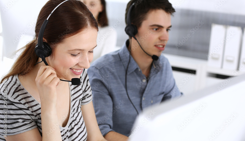Group of operators at work. Call center. Focus on beautiful woman receptionist in headset at customer service. Business concept and casual striped clothing style