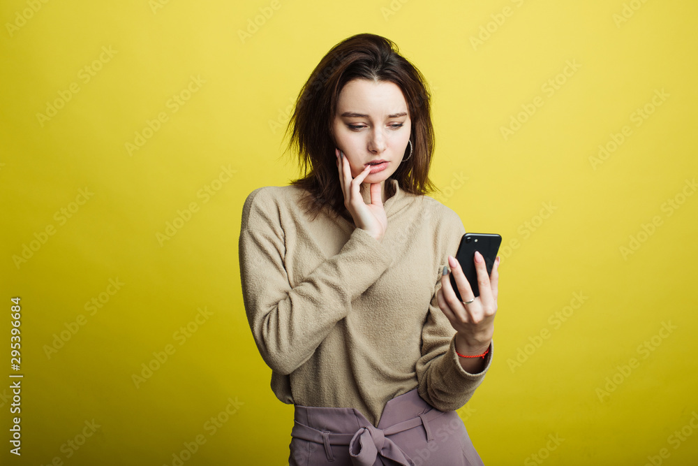 Image of happy young girl standing isolated on yellow background reading messages on phone Image of happy young girl standing isolated on yellow background reading messages on phone