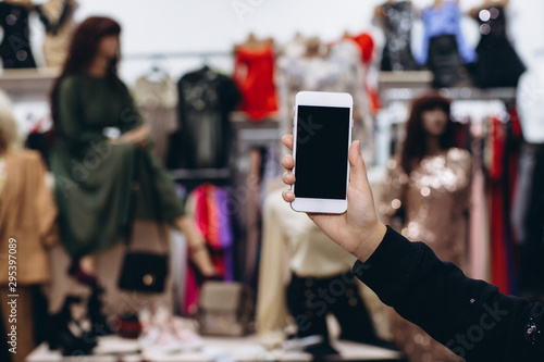 Female hand holding smartphone in clothes shop