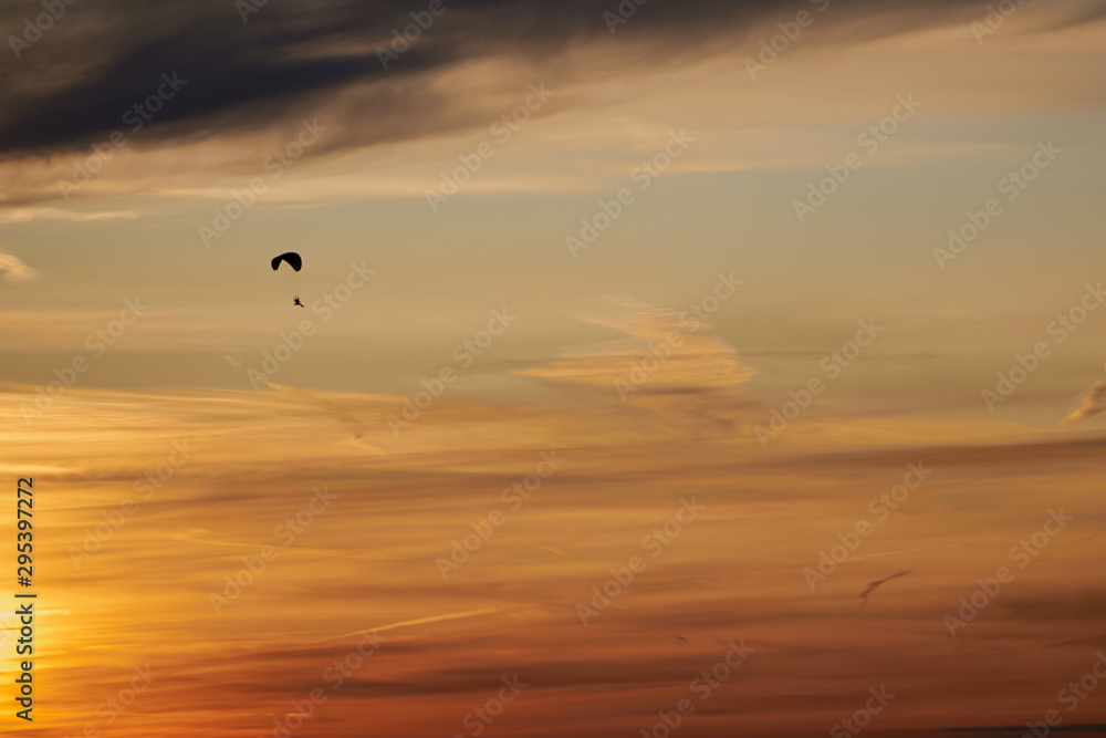 Skydiver flying in the evening sunset sky on a paraglider. There are Cirrus clouds in the sky. The sky is painted orange by the setting sun. Sports, Hobbies and passion. Background or backdrop.