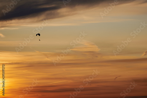 Skydiver flying in the evening sunset sky on a paraglider. There are Cirrus clouds in the sky. The sky is painted orange by the setting sun. Sports, Hobbies and passion. Background or backdrop.