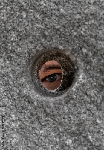 Open Eye Looking Through Round Hole In Stone Wall