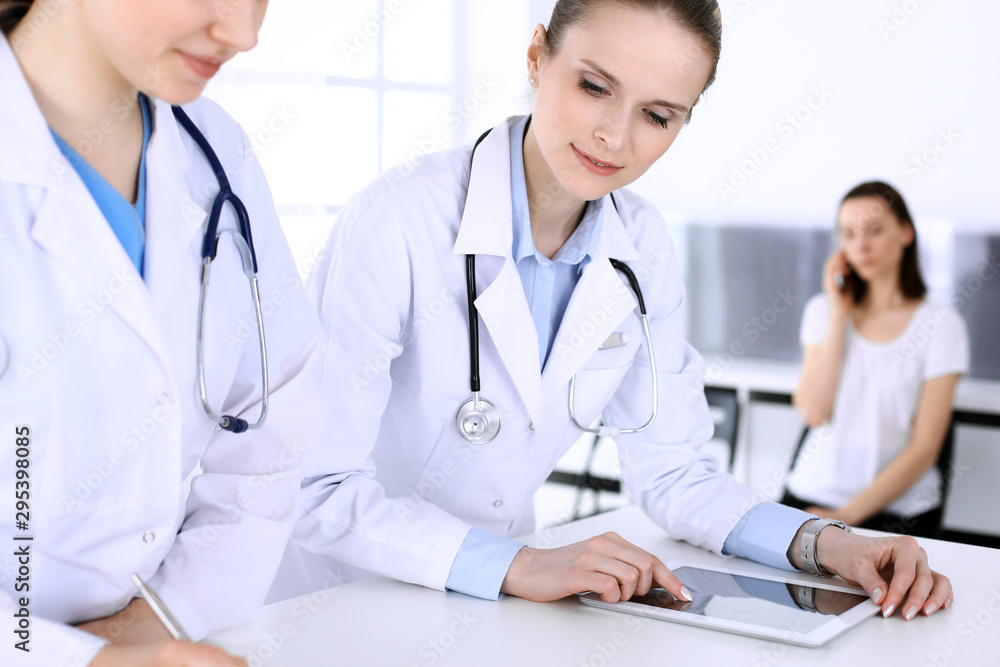 Group of doctors at work in hospital with patient in a queue at the background. Physician filling up medical documents or prescription while standing at reception desk. Data in medicine and health Group of doctors at work in hospital with patient in a queue at the background. Physician filling up medical documents or prescription while standing at reception desk. Data in medicine and health
