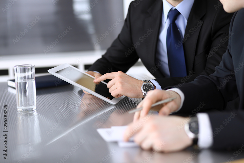 Businessman using tablet computer and work together with his colleague or partner at the glass desk in modern office, close-up. Unknown business people at meeting. Teamwork and partnership concept Businessman using tablet computer and work together with his colleague or partner at the glass desk in modern office, close-up. Unknown business people at meeting. Teamwork and partnership concept