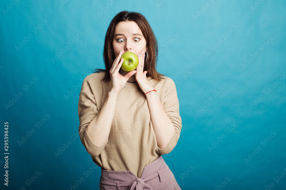 Fototapeta premium Image of a happy young girl standing on a blue background holding a green apple
