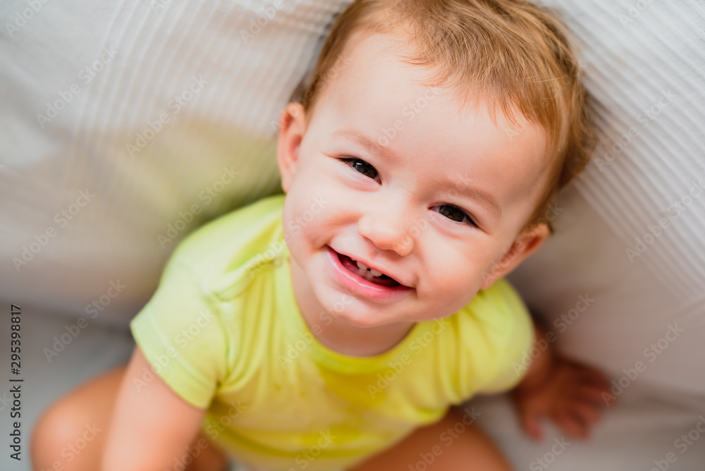 Portrait of a smiling baby looking up sitting on the floor with his first teeth.
