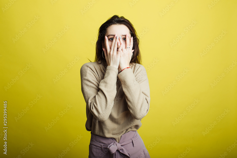 An image of a happy young girl standing isolated on a yellow background covered her face with her hands An image of a happy young girl standing isolated on a yellow background covered her face with her hands
