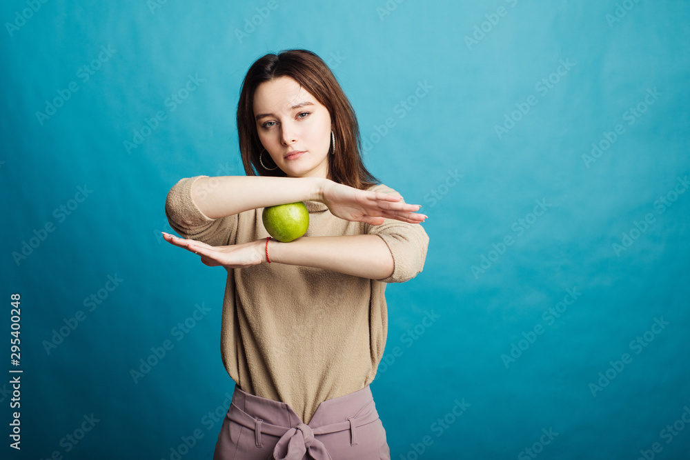 Image of a happy young girl standing on a blue background holding a green apple Image of a happy young girl standing on a blue background holding a green apple