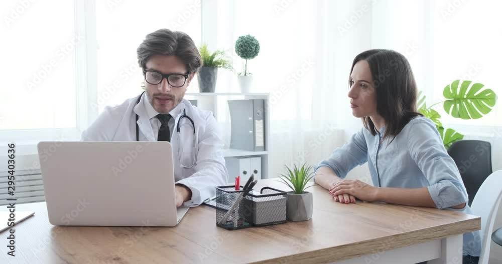Doctor working on laptop and showing xray report to woman patient at clinic Doctor working on laptop and showing xray report to woman patient at clinic