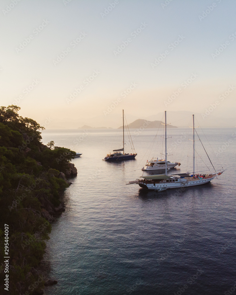 Evening sunset on the mediterranean sea. Luxury yachts lined up along the Turkish coastline, islands can be seen in the distant background. Beautiful scene shot aerially from a drone.
