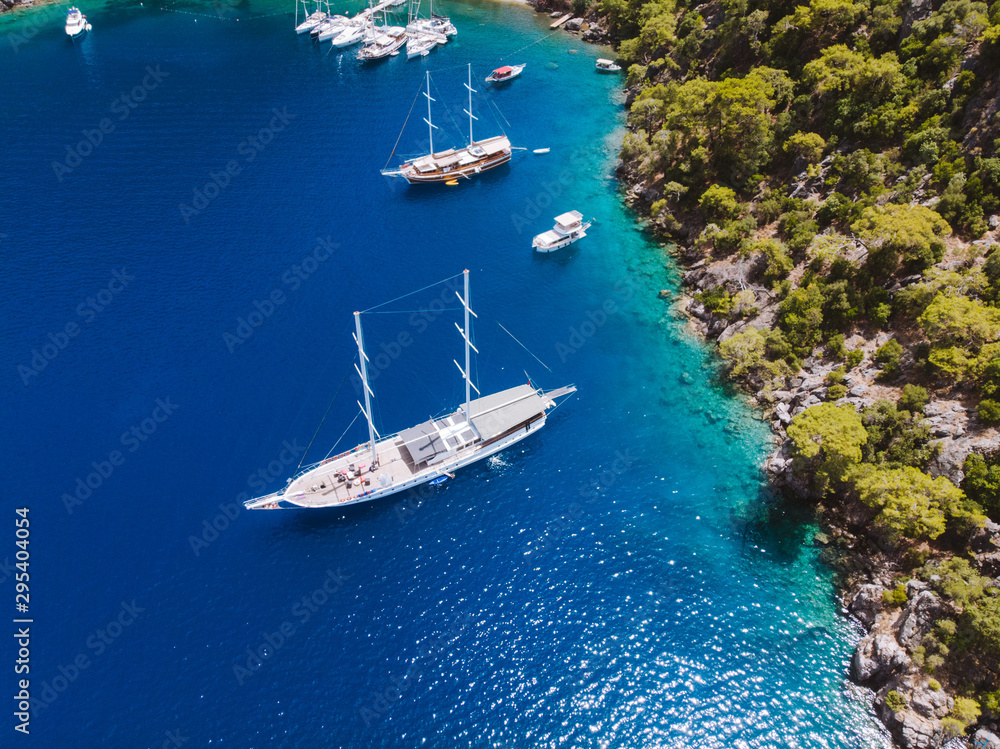 Naklejka premium Aerial drone perspective of luxury Turkish gulets and yachts in the deep blue and turquoise waters of the mediterranean sea. The bay and cliffs protect the boats from the strong winds.