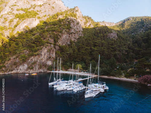 Aerial drone perspective of luxury Turkish gulets and yachts in the deep blue and turquoise waters of the mediterranean sea. The bay and cliffs protect the boats from the strong winds. © Dylan Alcock