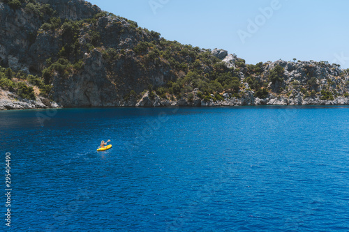 A lone girl paddling a yellow kayak in remote mediterranean waters, exploring the Turkish coastline. Beautiful blue water and coastline with amazing visibility. Shot aerially with a drone. © Dylan Alcock