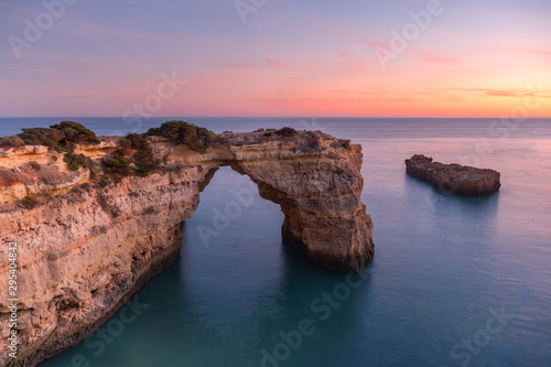 Algarve beach at sunset. Loving moment under natural arch carved in stone is a tourist attraction of the south coast of Portugal. Panoramic view from the cliff.