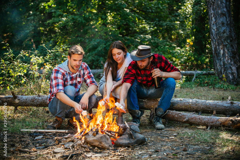 Group of friends camping with marshmallows over a camp fire. Spring or autumn camping. Picnic time. Young people eating roasted marshmallows while camping near campfire. Summer lifestyle. Group of friends camping with marshmallows over a camp fire. Spring or autumn camping. Picnic time. Young people eating roasted marshmallows while camping near campfire. Summer lifestyle.