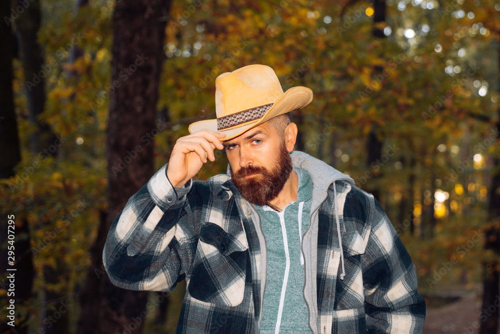 Obraz premium Handsome charming beard man in freezing cold in the autumn forest, wearing a cawboy hat. Traditions and reliability, good manners. Concept of employing seasonal workers.