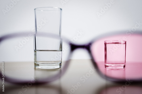 Принти на полотні Optimism, illustrated by comparing less than half full glass in one frame of glasses with full smaller glass through rose tinted lens in another frame