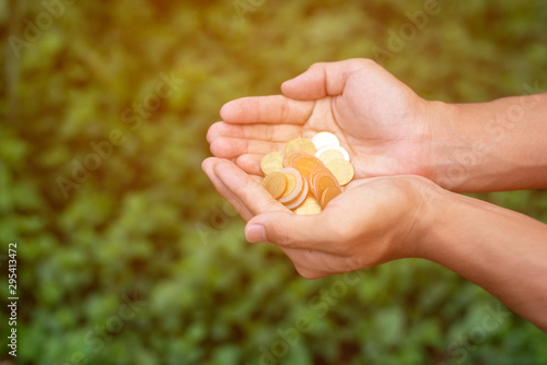 hai currency coins Baht on the hand of a person with a natural green background that is blurred to save money.