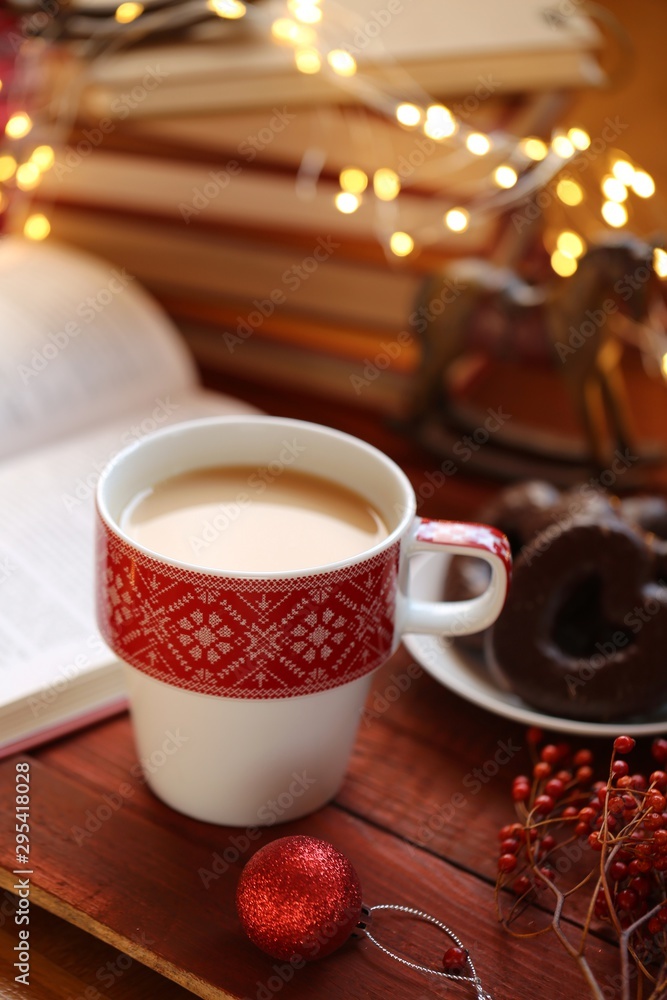 Obraz premium Winter tea. Winter books. cup of tea, books, Christmas gingerbread cookies, decor and a shining garland on a red wooden background.Books about Christmas. Winter holidays.
