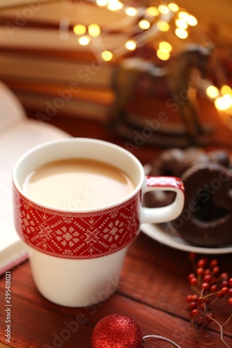 Winter tea. Winter books. A cup of hot tea, books, Christmas gingerbread cookies, decor and a shining garland on a red wooden background.Books about Christmas. 