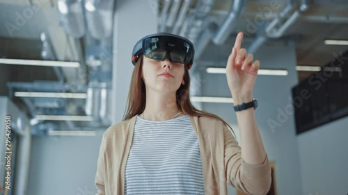 Young Hipster Woman in Holographic Augmented Reality Glasses Standing in Empty Office and Map it. She's Moving Virtual Pieces Around the Space. Room Has Tracking Points for Video Software. photo