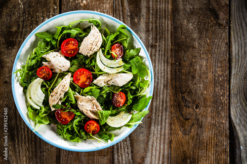 Salad with chicken meat and arugula on wooden table