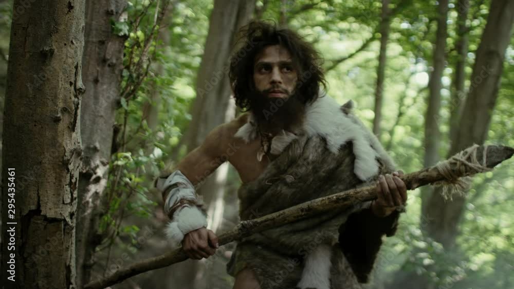 Portrait of Primeval Caveman Wearing Animal Skin and Fur Hunting with a Stone Tipped Spear in the Prehistoric Forest. Prehistoric Neanderthal Hunter Ready to Throw Spear in the Jungle Portrait of Primeval Caveman Wearing Animal Skin and Fur Hunting with a Stone Tipped Spear in the Prehistoric Forest. Prehistoric Neanderthal Hunter Ready to Throw Spear in the Jungle