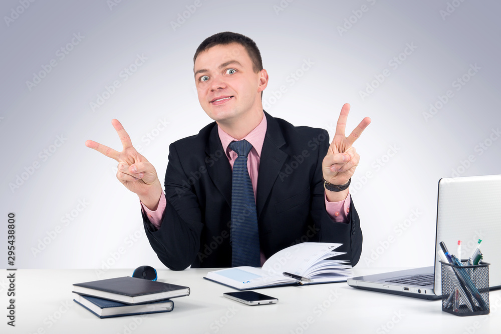 Young business man showing victory sign on grey background Young business man showing victory sign on grey background