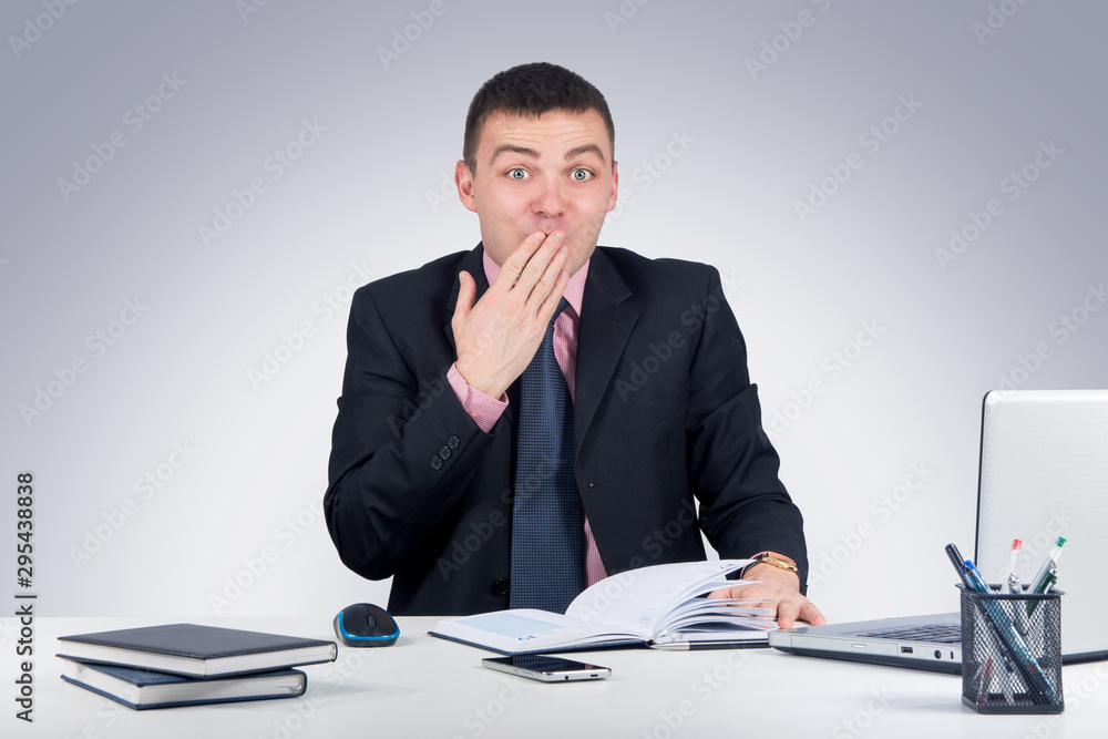 Young business man sitting at the office and looking shocked at the camera covering his mouth with his hand Young business man sitting at the office and looking shocked at the camera covering his mouth with his hand