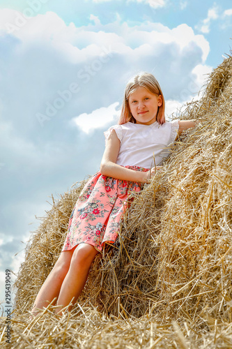 A girl with long flowing hair in a pink dress climbed on large bales of straw