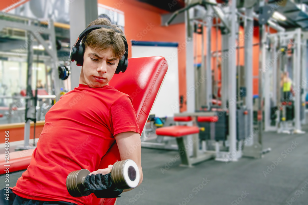 Obraz premium cute young man in sports clothes and headphones is engaged with dumbbells in the gym