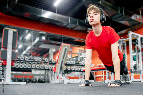 cute young man in sportswear and headphones doing push-ups in the gym