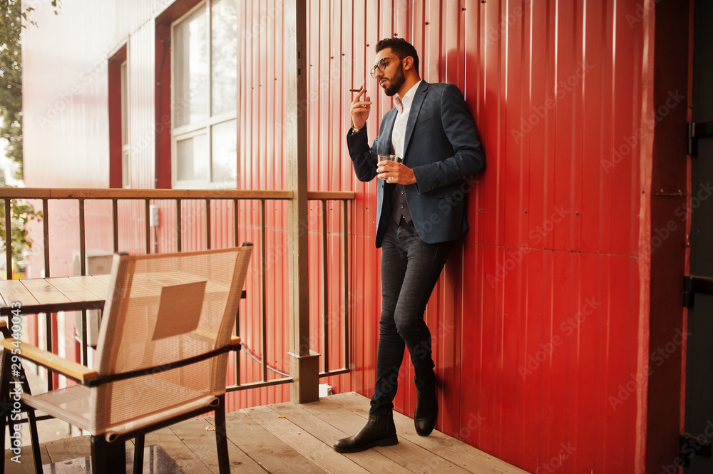 Handsome well-dressed arabian man smoke cigar with glass of whiskey at balcony of pub. Handsome well-dressed arabian man smoke cigar with glass of whiskey at balcony of pub.